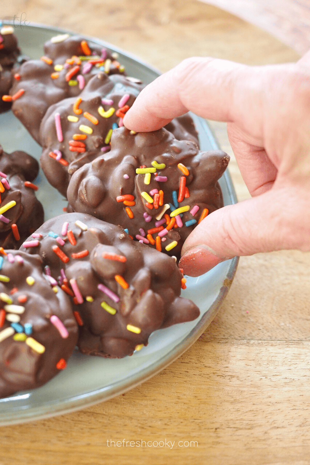 Crockpot Peanut Clusters on plate with rainbow sprinkles and hand grabbing one.