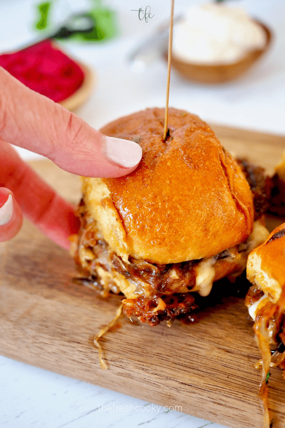 A hand grabbing a roast beef slider to eat.