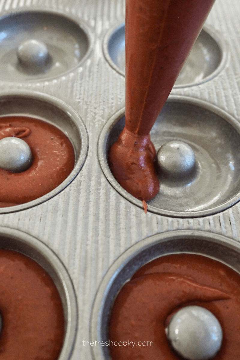 Piping red velvet donuts into donut pan. 