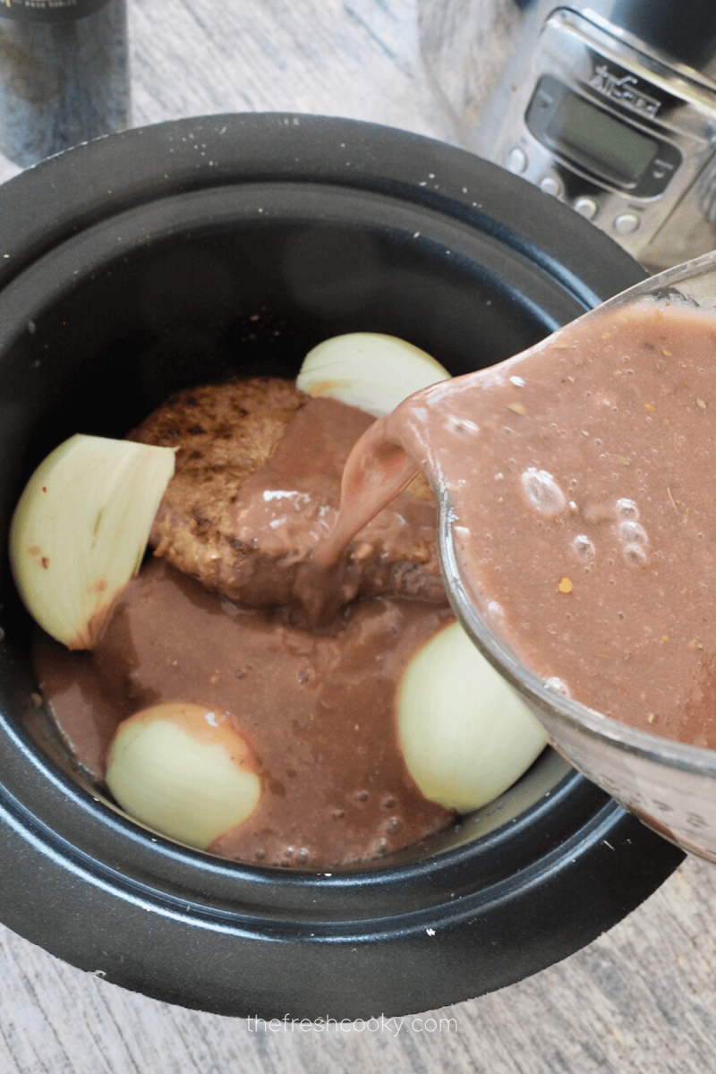 Pouring red wine gravy mixture over the top of crockpot London Broil.