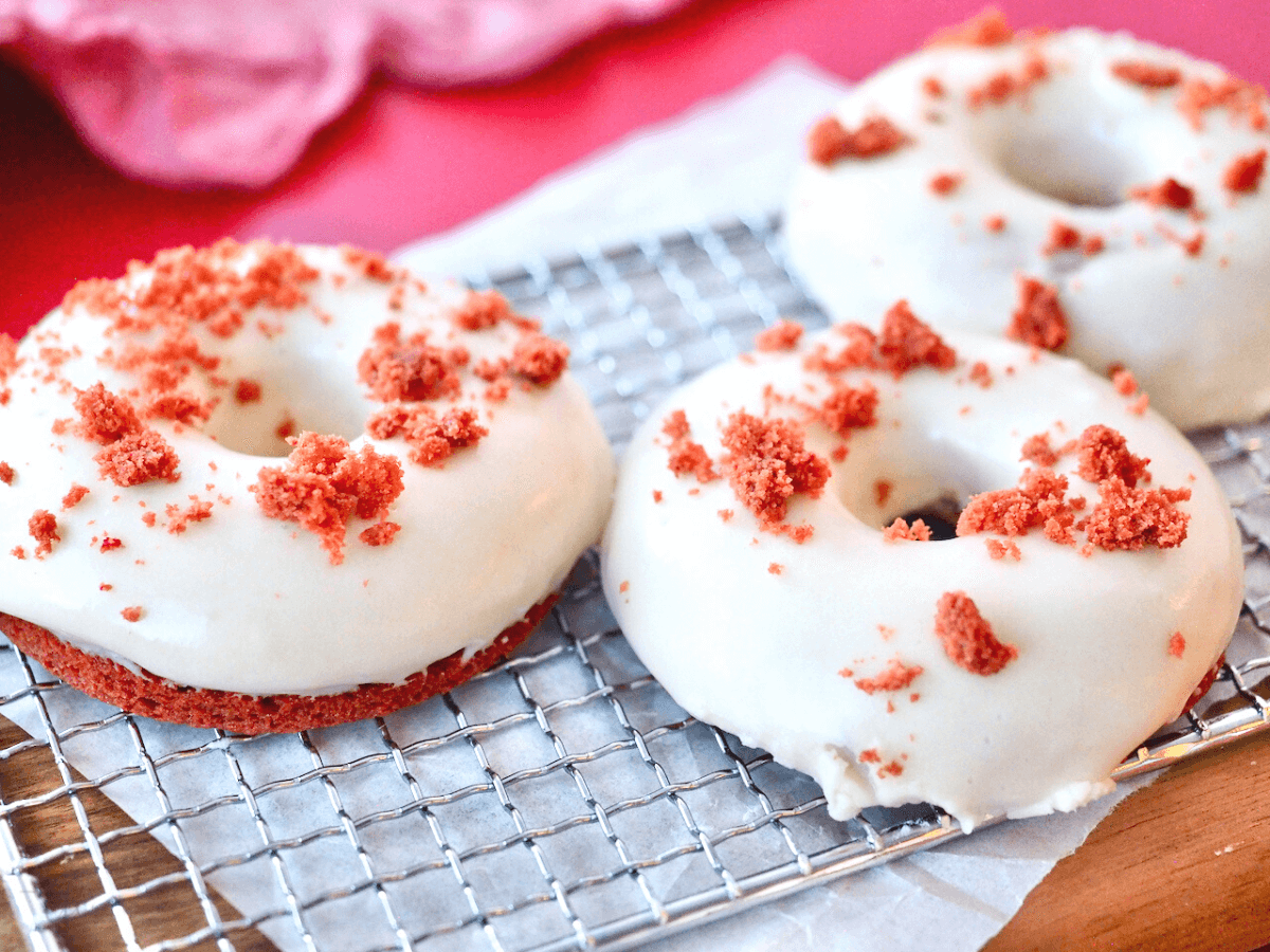 Red Velvet donuts on wire rack, topped with crumbled red velvet cake.