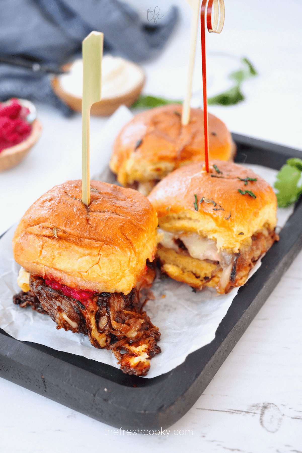 Roast Beef sliders with caramelized onions, melting cheese on a tray with picks in them.