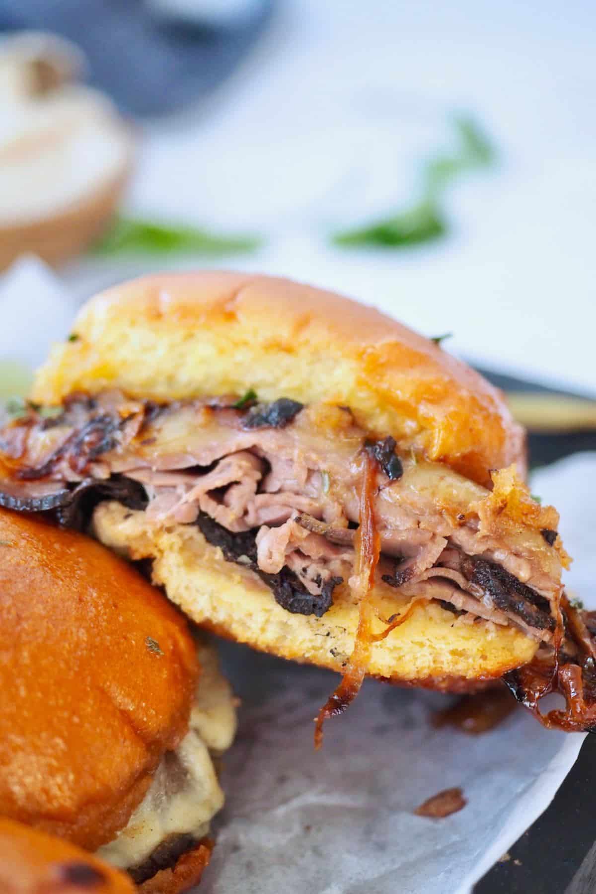 Close up of layers of roast beef with onions and melty cheese on slider buns.