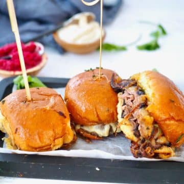 Three roast beef sliders with picks sitting on a tray to serve.