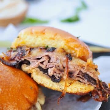 Close up of layers of roast beef on Hawaiian slider buns with melty cheese.