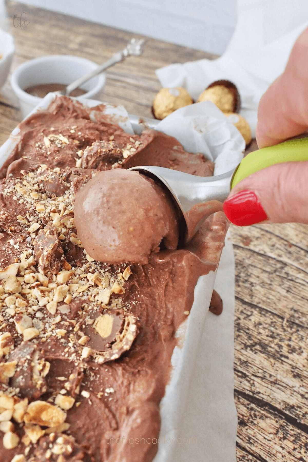 Ferrero Rocher Ice Cream in pan with hand using ice cream scoop and scooping a big scoop to put into a bowl.