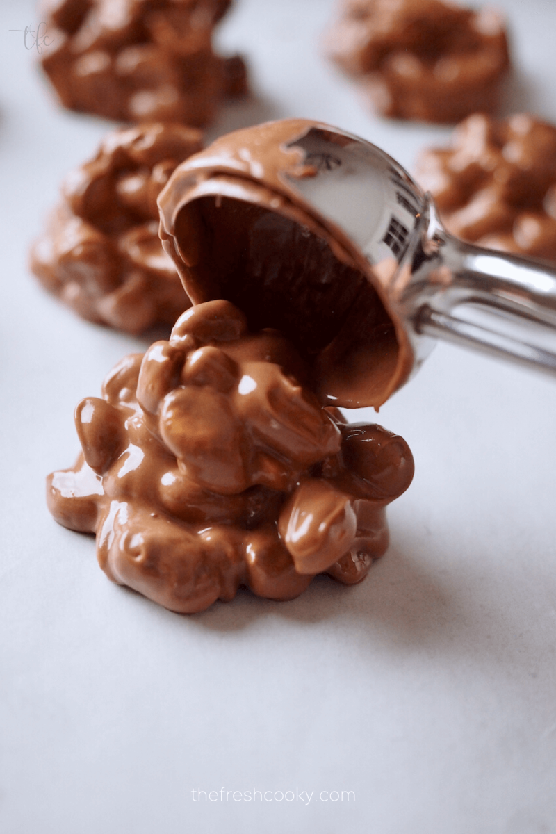 Scooping crockpot peanut clusters onto parchment lined baking sheet. 