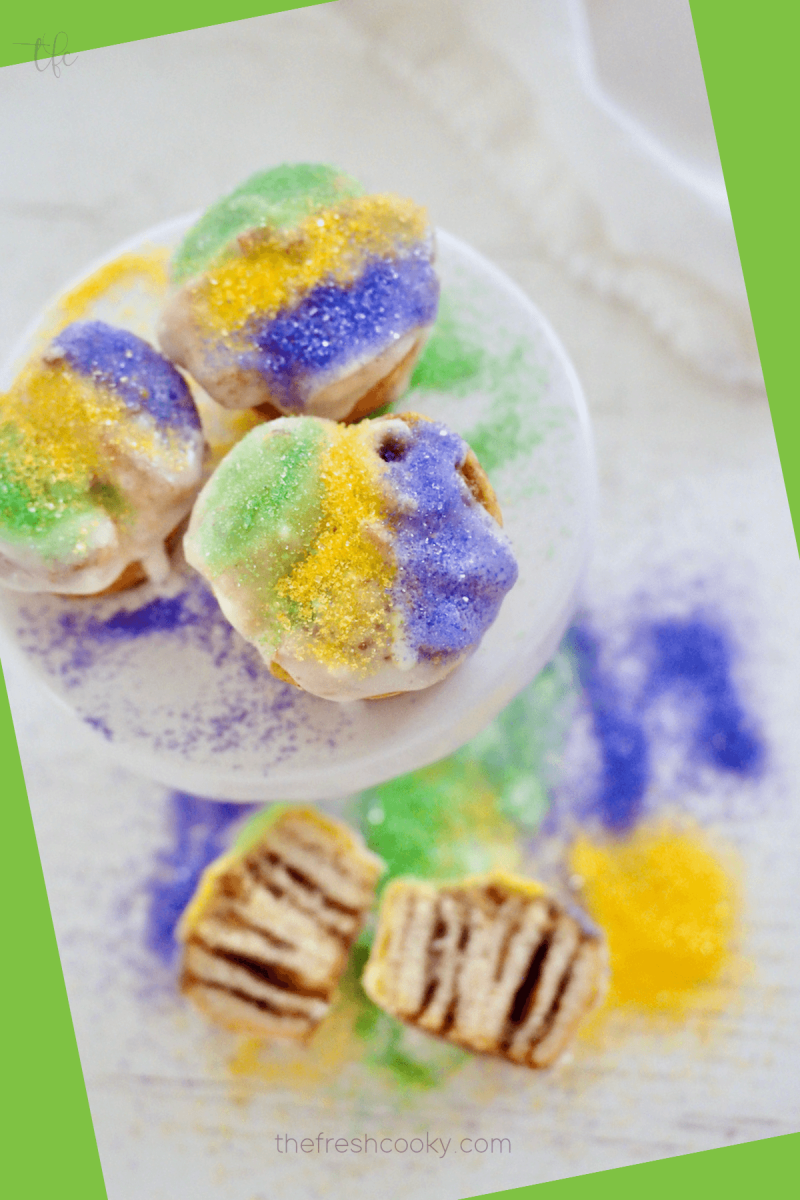 Easy Mini king cakes with three king cakes on a pedestal and one cut in half revealing the cinnamon sugar insides.