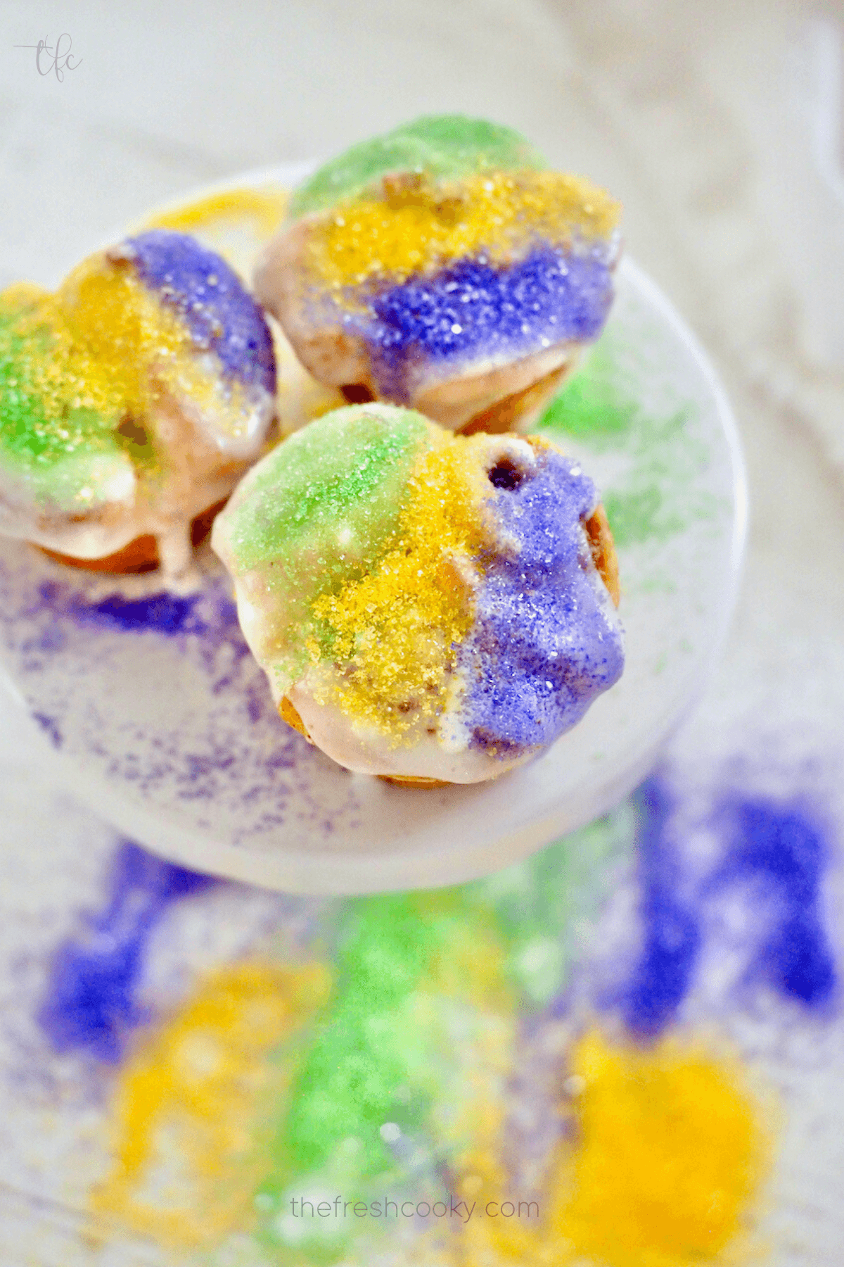 Easy Mini King Cakes recipe with crescent rolls three on a small pedestal with yellow, purple and green sugars for Mardis gras.