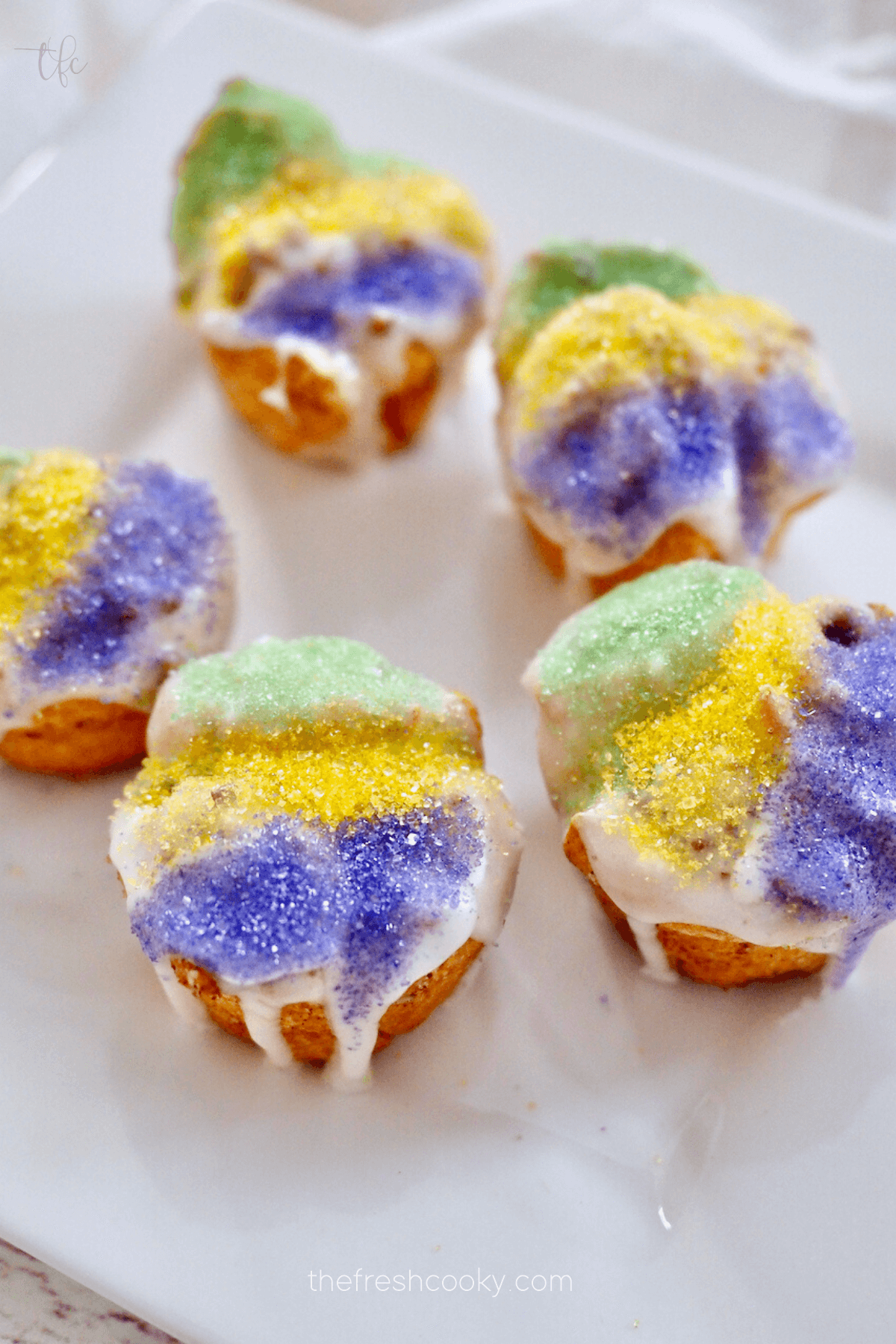 Easy mini king cake recipe with crescent rolls on a square white plate, decorated with green, yellow and purple Mardis gras sugars.