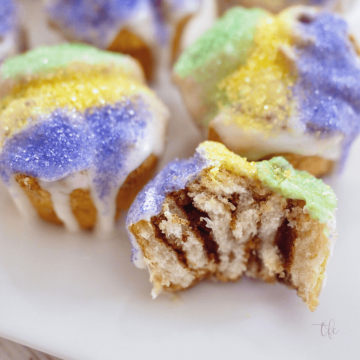 Easy Mini King Cake Recipe with Crescent Rolls, square image with bite take out of one cake revealing cinnamon sugar swirl.