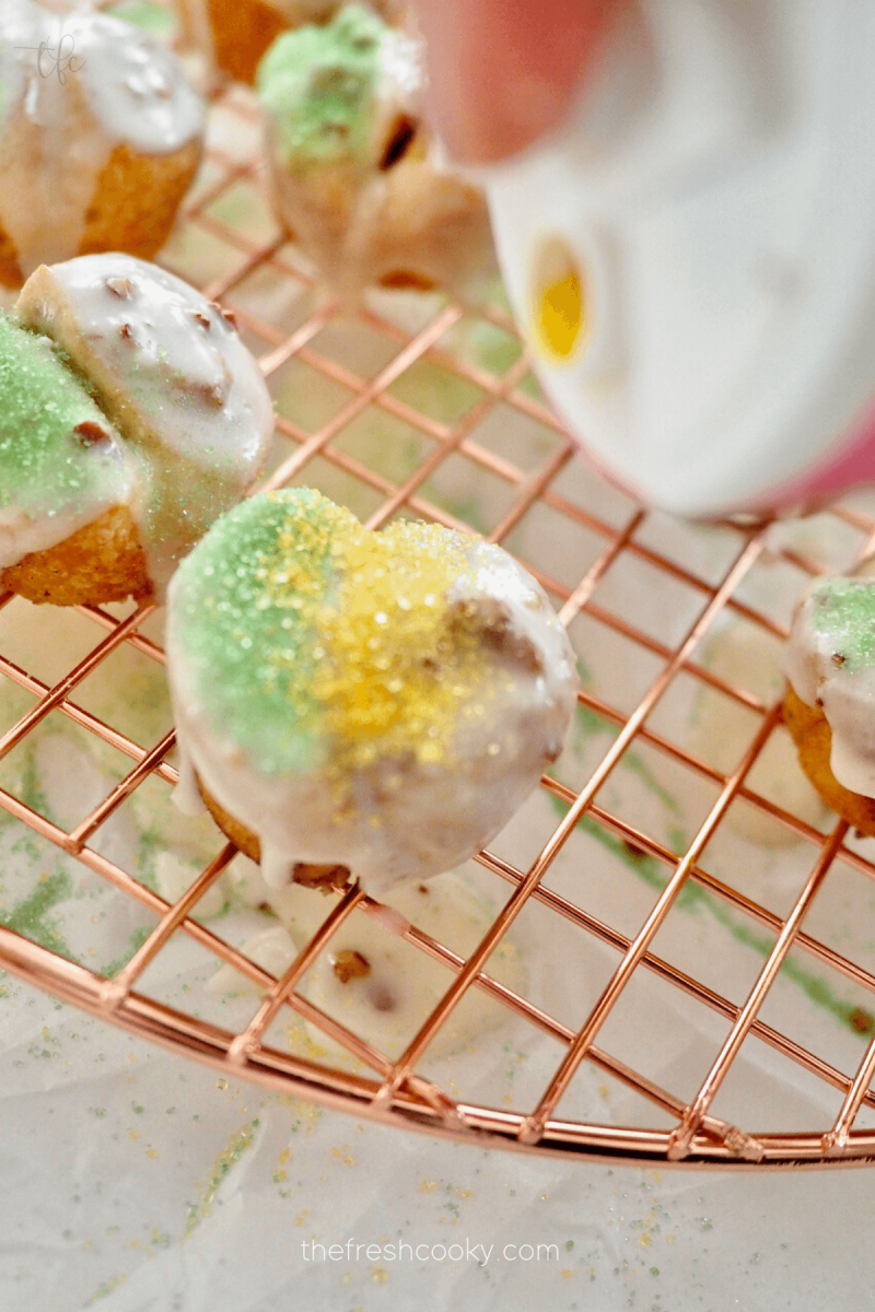 Sprinkling on yellow sugar alongside green sugar on mini king cakes. 