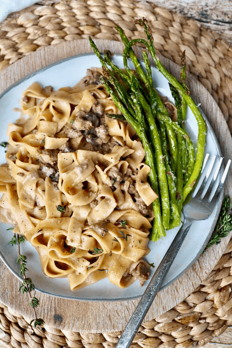 Instant Pot ground beef stroganoff on pretty plate with stalks of fresh roasted asparagus and a rustic fork.