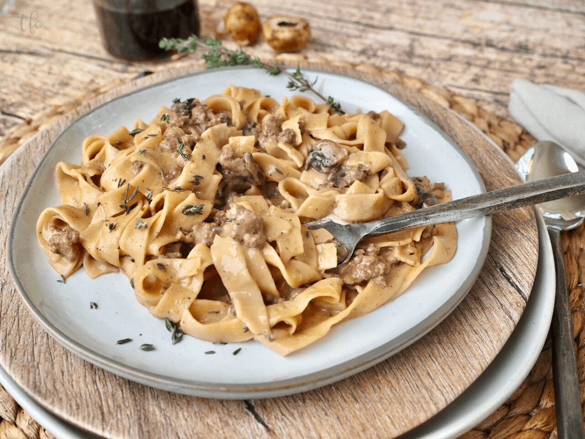Instant Pot Ground Beef Stroganoff on plate, with noodles swirled around fork and glass of wine in background.
