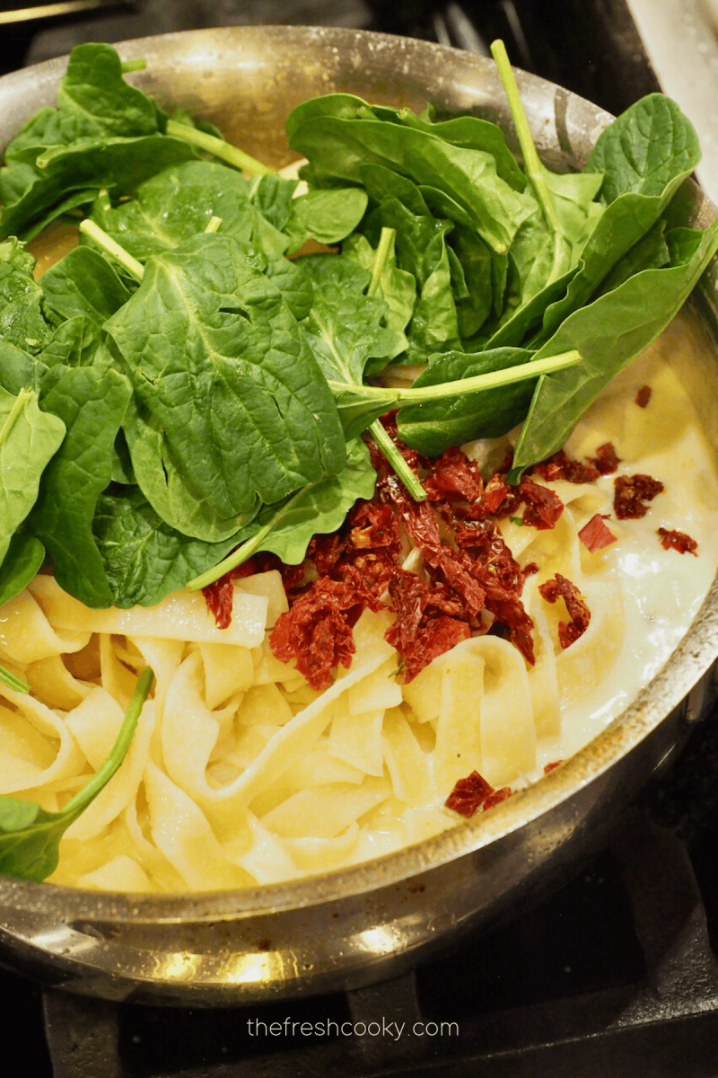 Adding baby spinach and sun-dried tomatoes to fettuccine alfredo. 