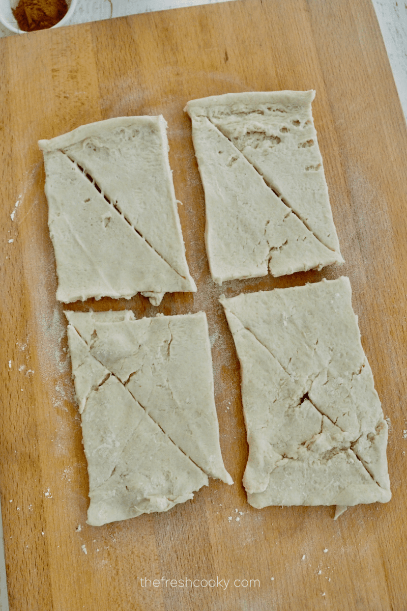 Crescent roll dough separated into rectangles on cutting board. 