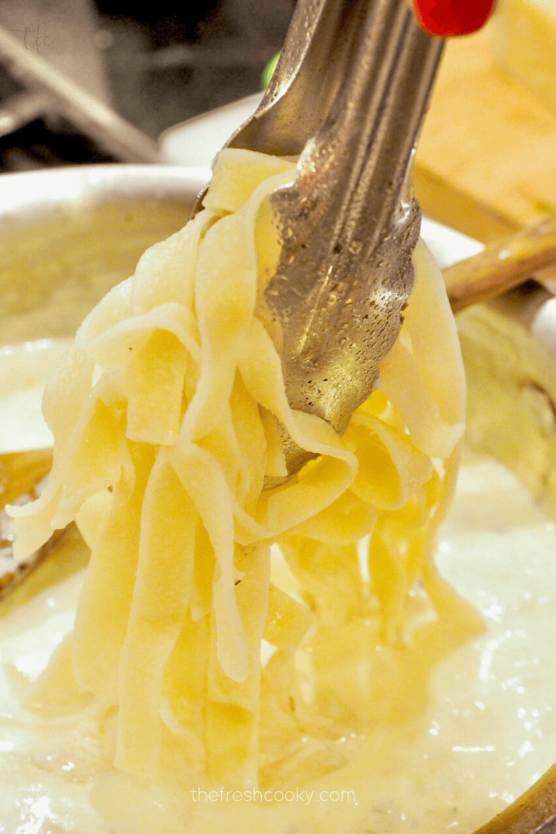 Tossing cooked fettuccine in Alfredo sauce. 