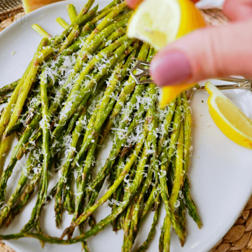 Hand squeezing lemon on fresh air fryer roasted asparagus.