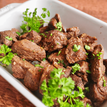 Air Fryer Steak Tips in casserole dish garnished with curly parsley.