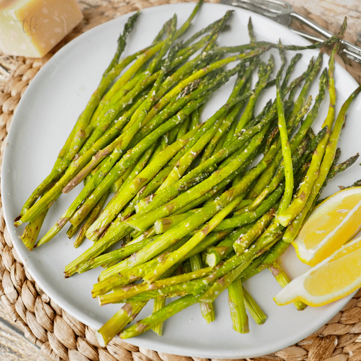 Square image of top down shot of air fryer asparagus on a plate with lemons and fresh block of parmesan. 