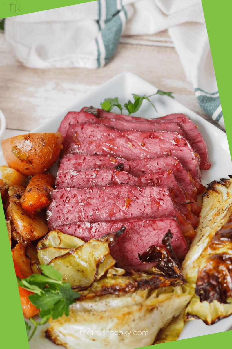 Pin for baked corned beef and cabbage recipe with close up of corned beef sliced on a plate with vegetables.