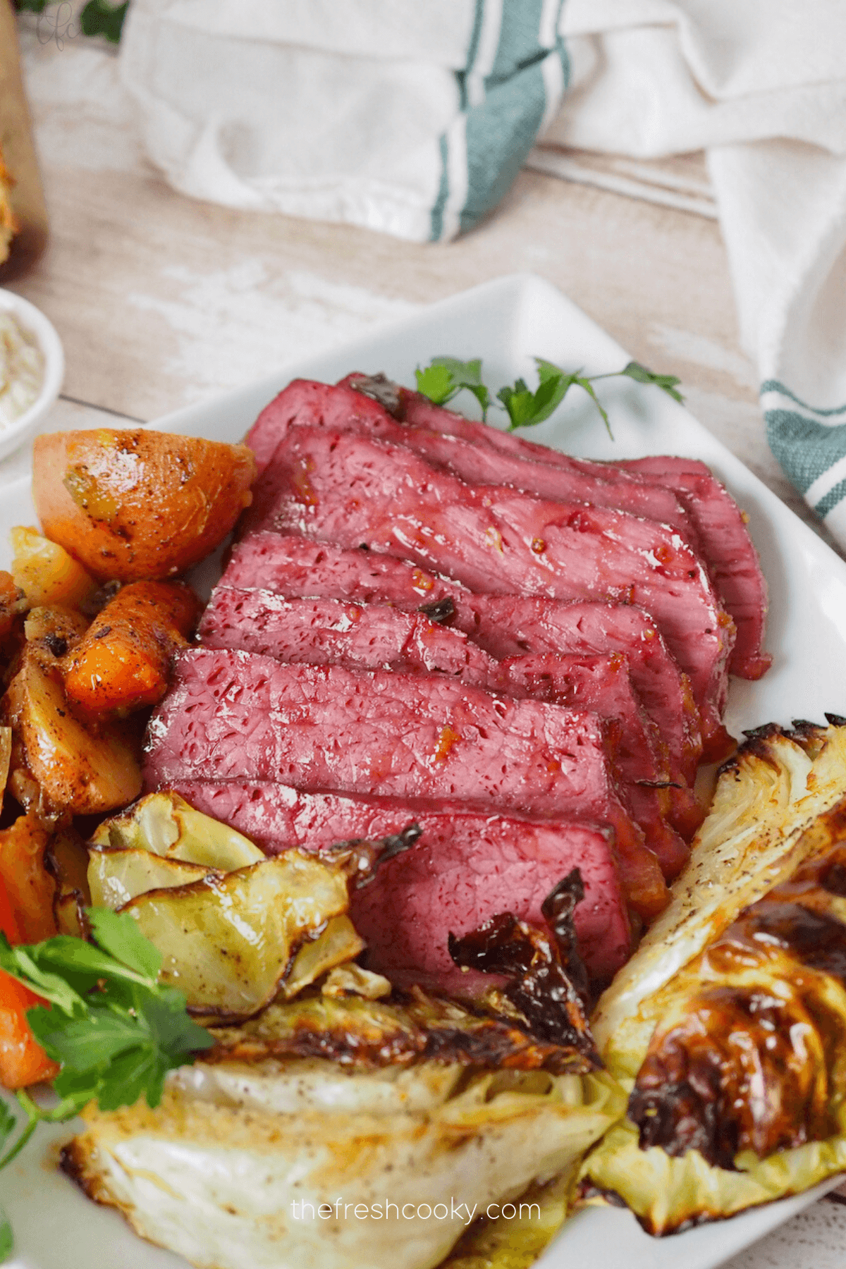 Baked corned beef recipe on platter sliced with roasted cabbage, potatoes and carrots.