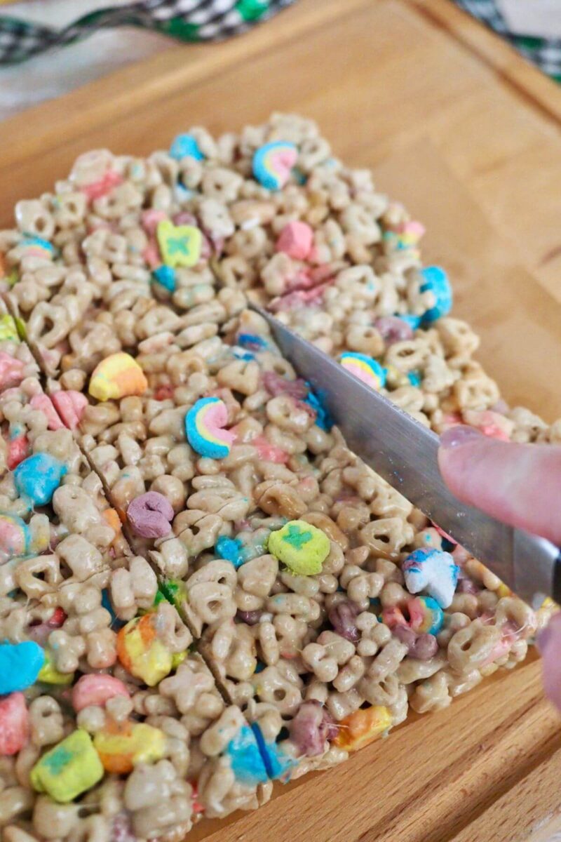 Hand on knife, slicing the Lucky Charms treats into squares or bars.