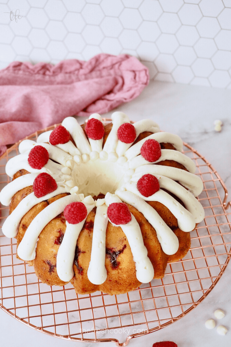 Frosting white chocolate raspberry bundt cake with fresh raspberries on top and white chocolate chips.