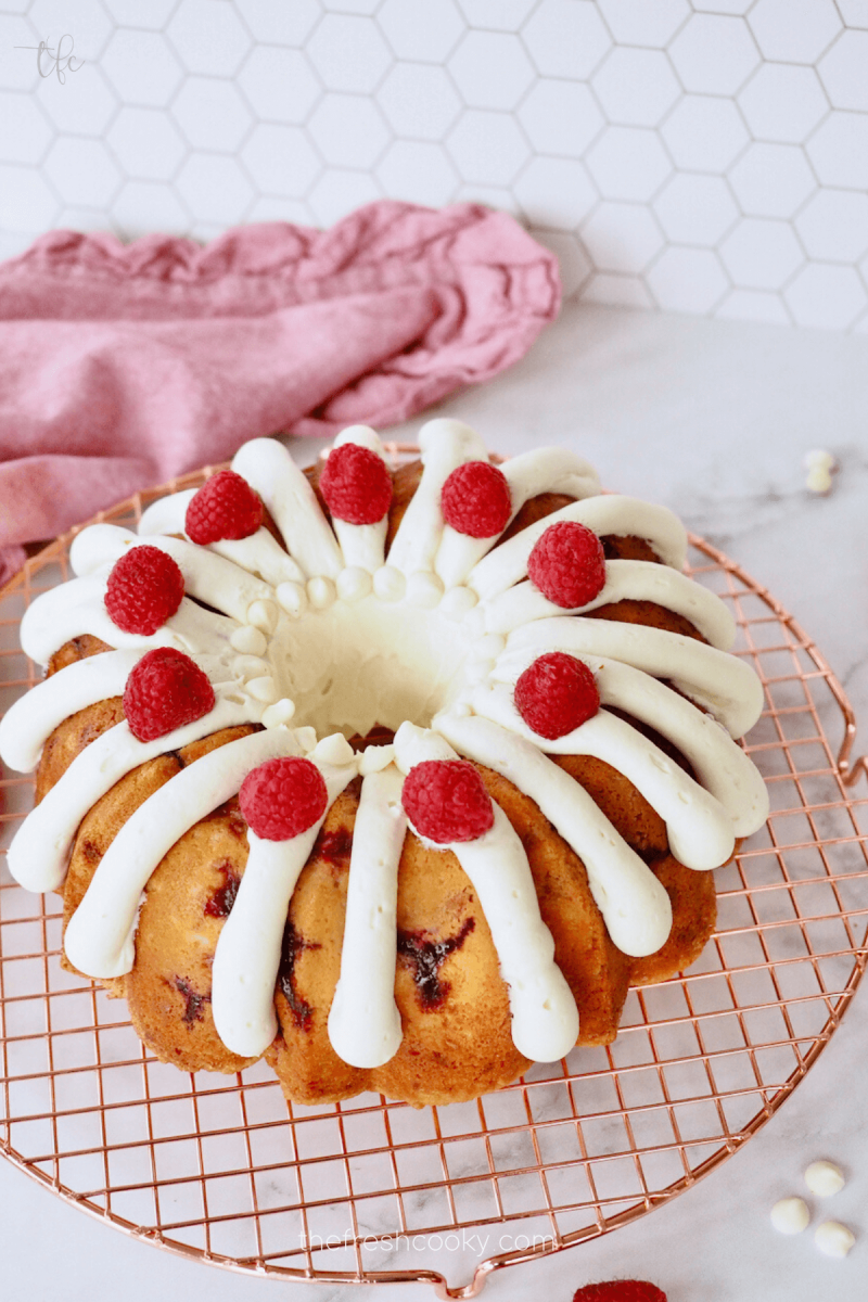 https://www.thefreshcooky.com/wp-content/uploads/2022/03/Frosted-and-decorated-White-Chocolate-Raspberry-Bundt-Cake-800x1200.png