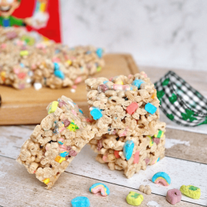 Lucky Charms Bars stacked on table with brightly colored cereal marshmallows scattered around.