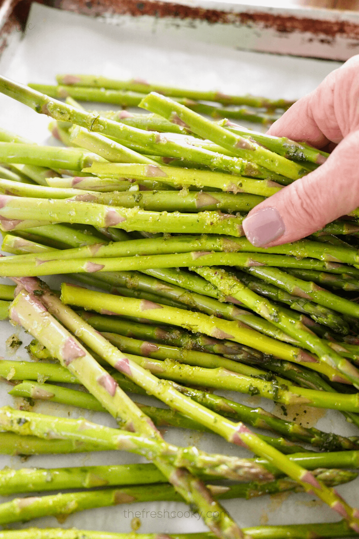 Using hands to toss the fresh asparagus in oil mixture for air fryer asparagus.