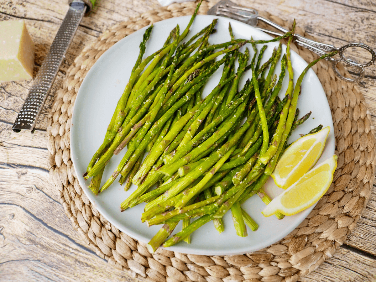 Top down shot of plated air fryer asparagus with lemon wedges, and block of parmesan with grater.