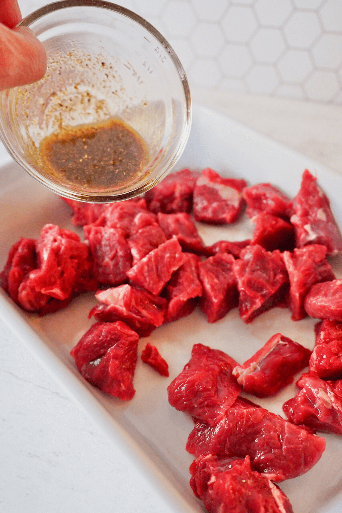 Pouring marinade mixture onto steak bites for air fryer.