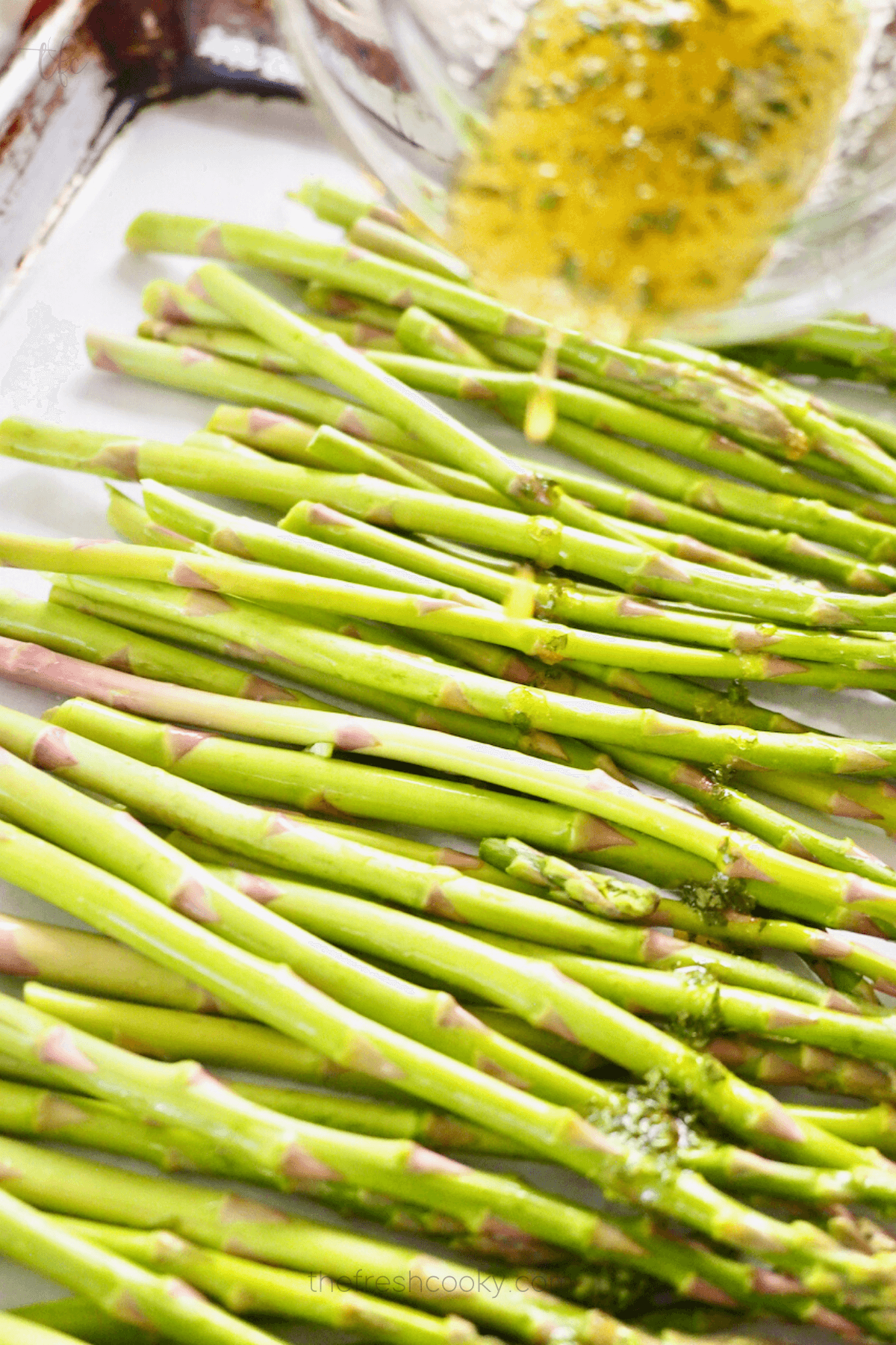 Pouring seasoning oil over the top of washed asparagus for air fryer asparagus recipe.