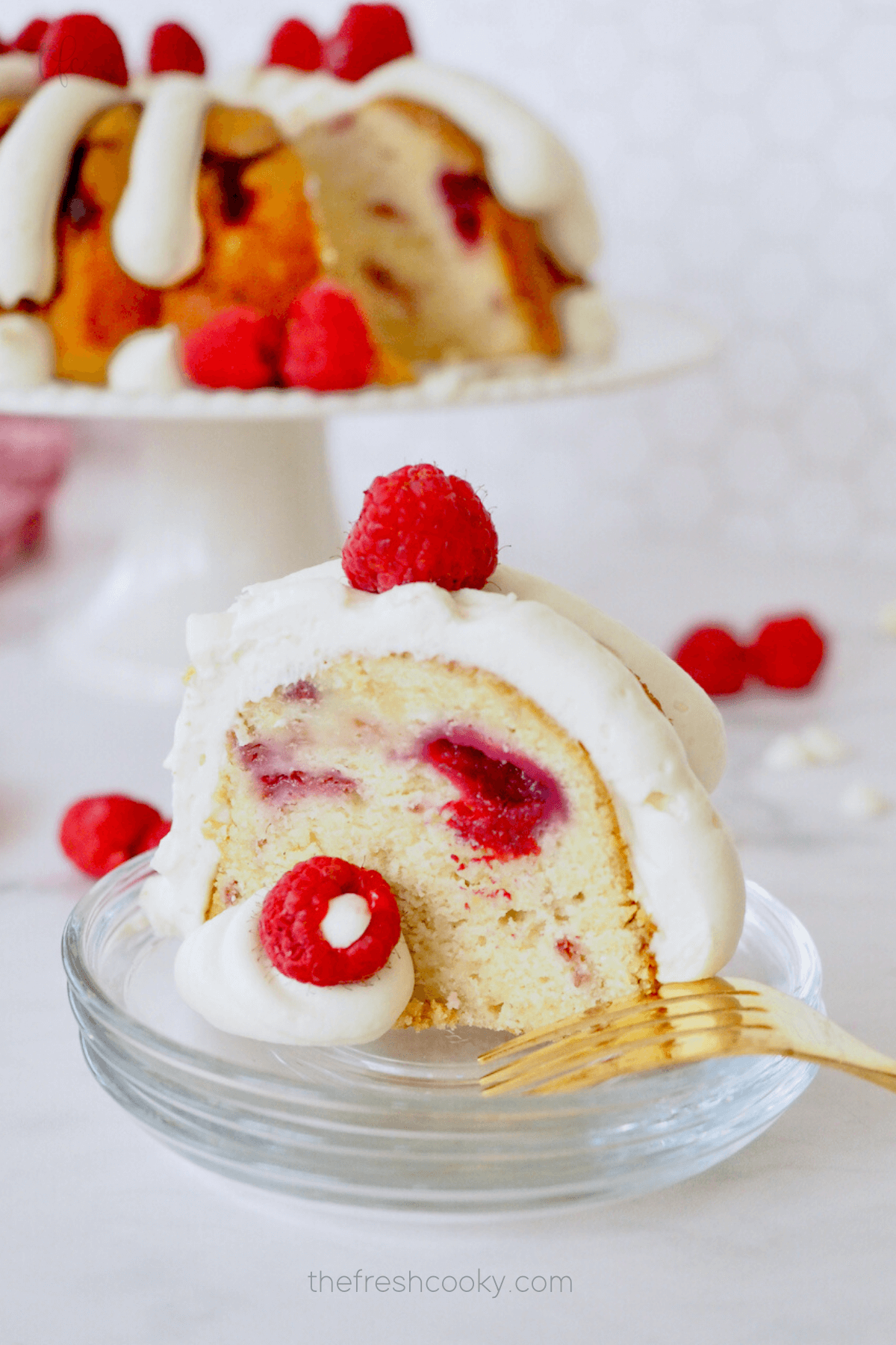 White Chocolate Raspberry bundt cake, slice on a plate with fresh raspberries and bundt cake in background. 