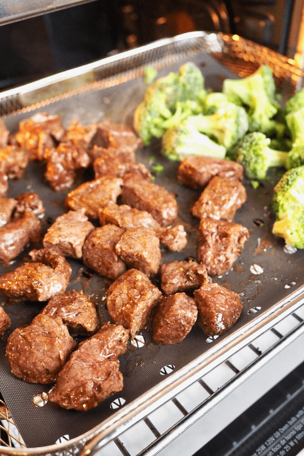 Steak tips in air fryer basket with added broccoli at the end. 