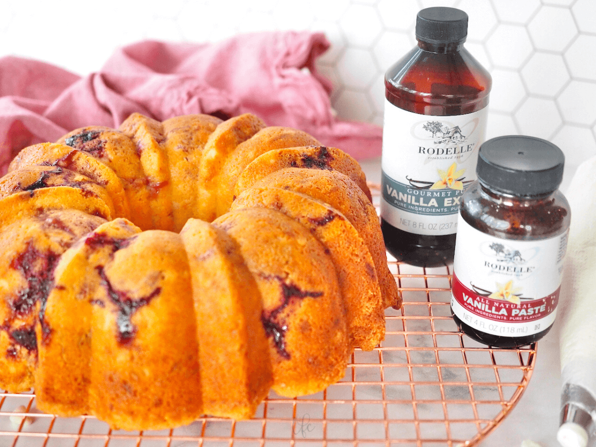 Rodelle vanilla and vanilla bean paste next to baked white chocolate raspberry bundt cake on cooling rack.