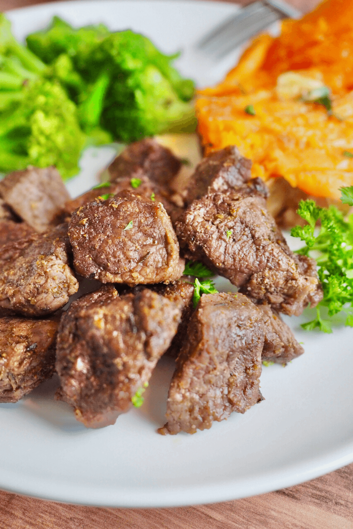 Air fryer steak tips on plate with fresh broccoli and baked sweet potato.