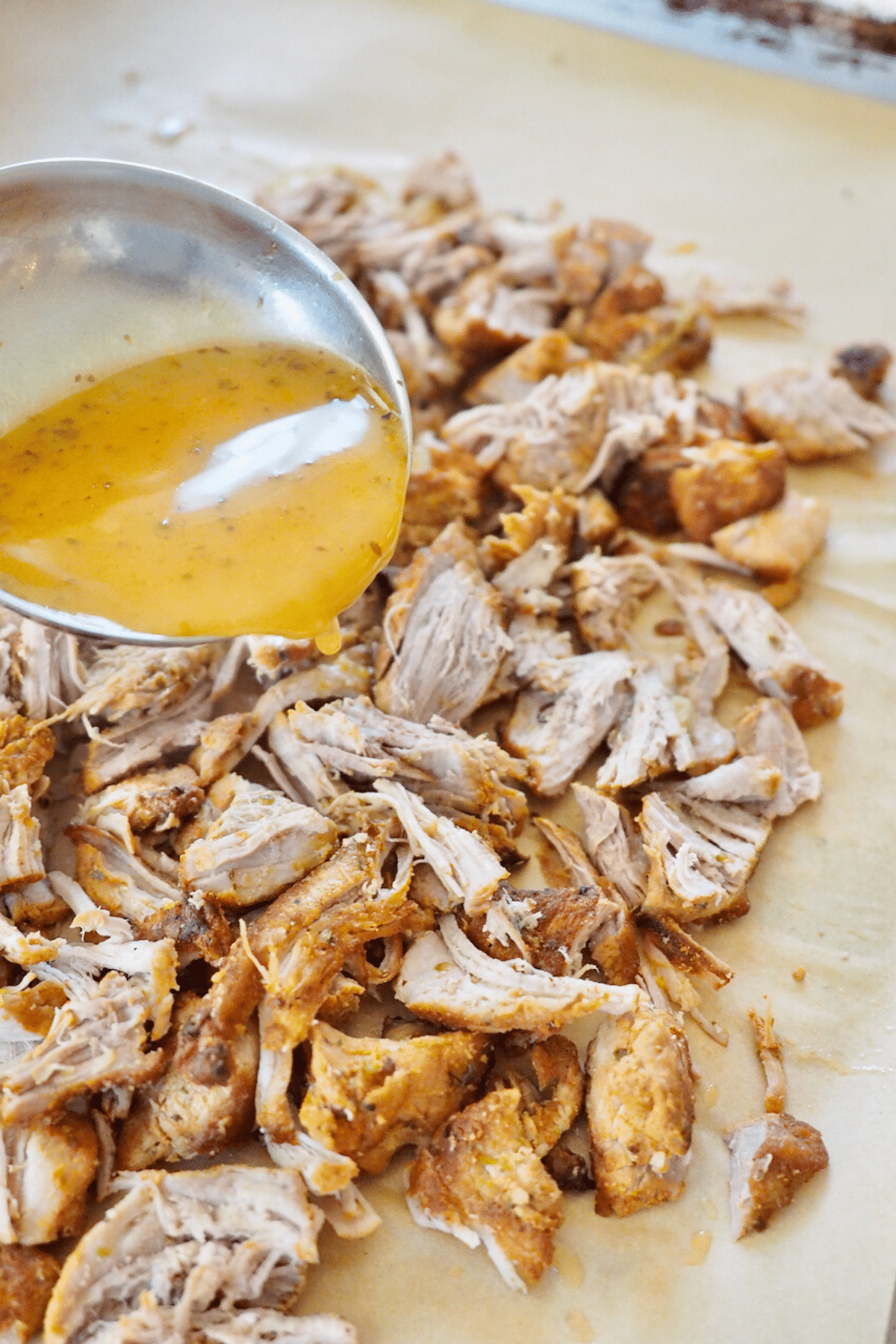 Pouring cooking juices over shredded carnitas on pan.