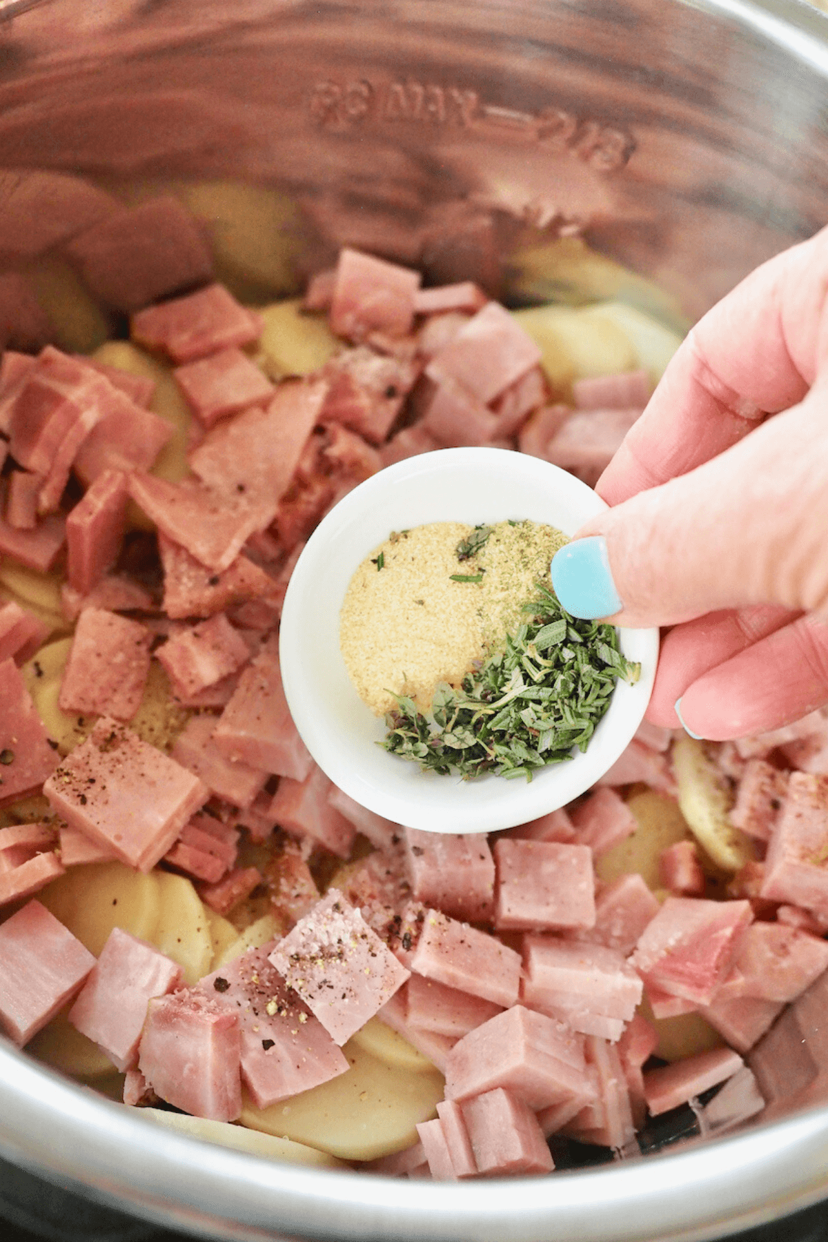 Herbs and spices being added to scalloped potatoes into Instant Pot.