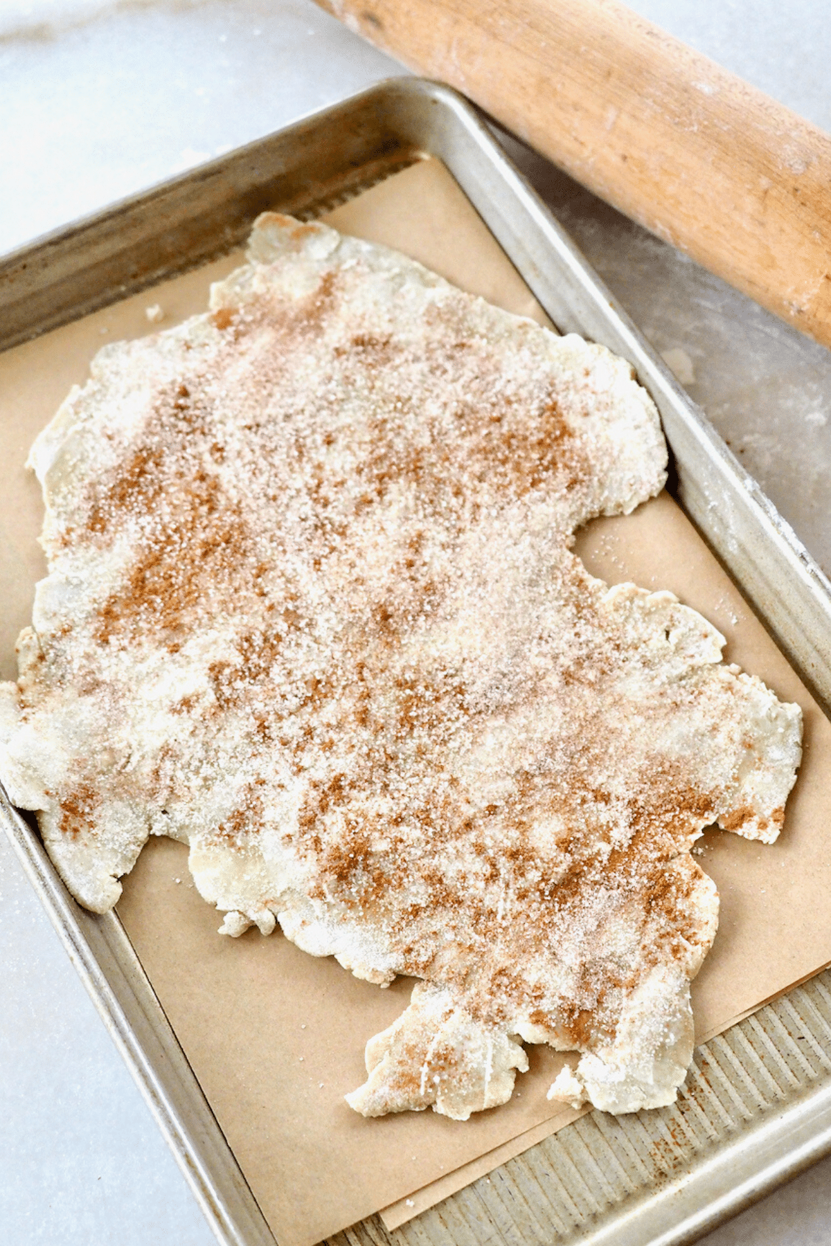 Pie dough rolled out and sprinkled with cinnamon sugar on baking sheet. 