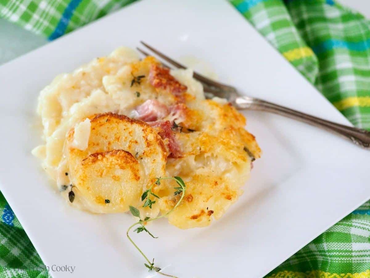 Serving of easy scalloped potatoes with ham on a square white plate, with a garnish of fresh thyme.