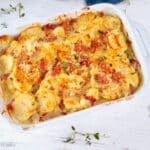 A white Staub baking dish filled with golden, cheesy, bubbly scalloped potatoes with ham.