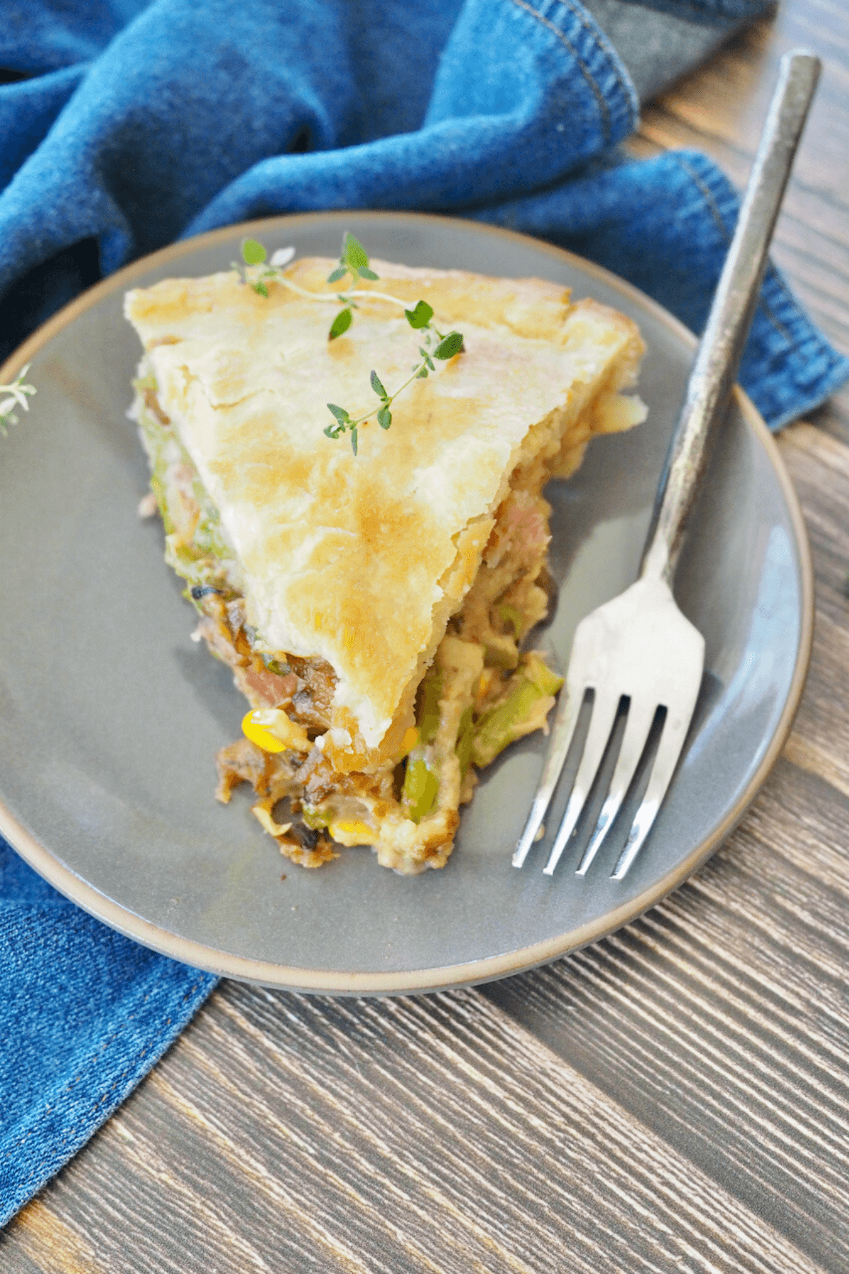 Slice of leftover ham pot pie on gray plate with rustic fork.