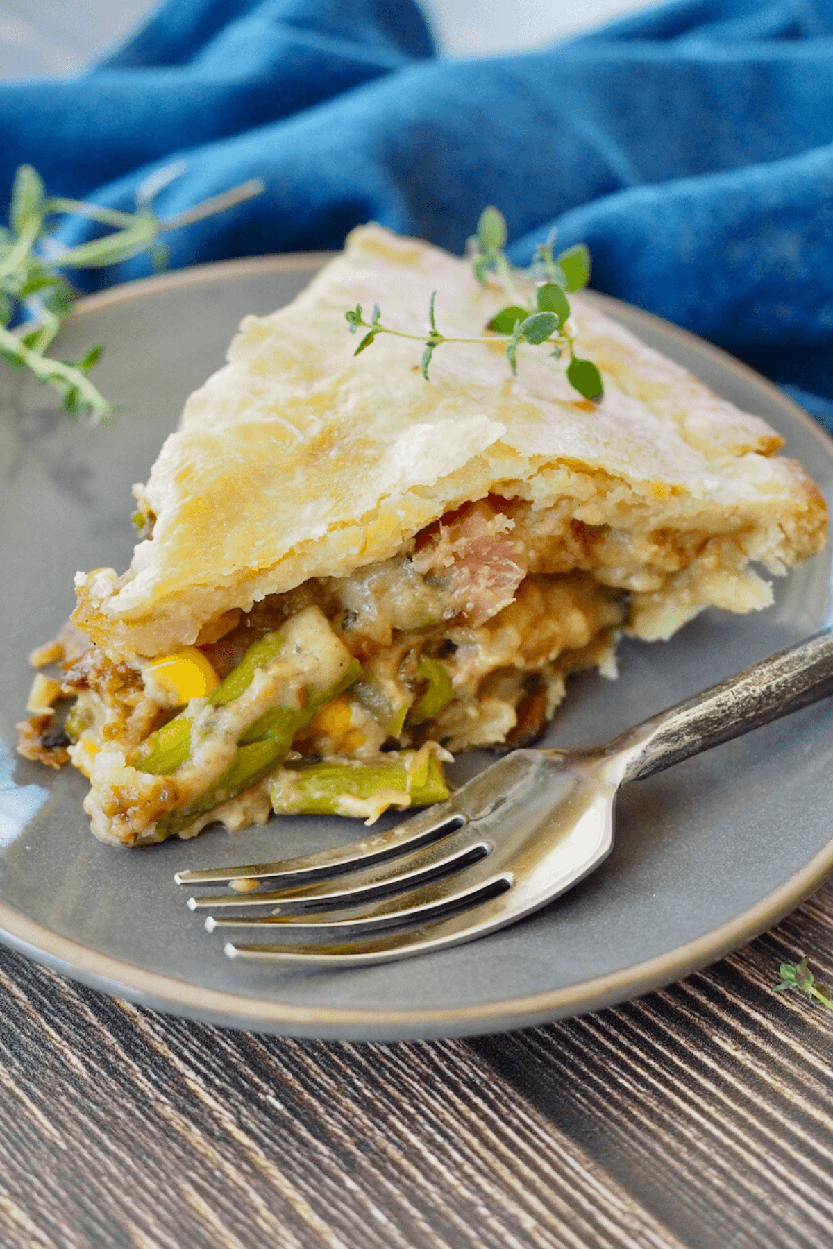 Slice of ham pot pie on a plate with a fork and fresh thyme.