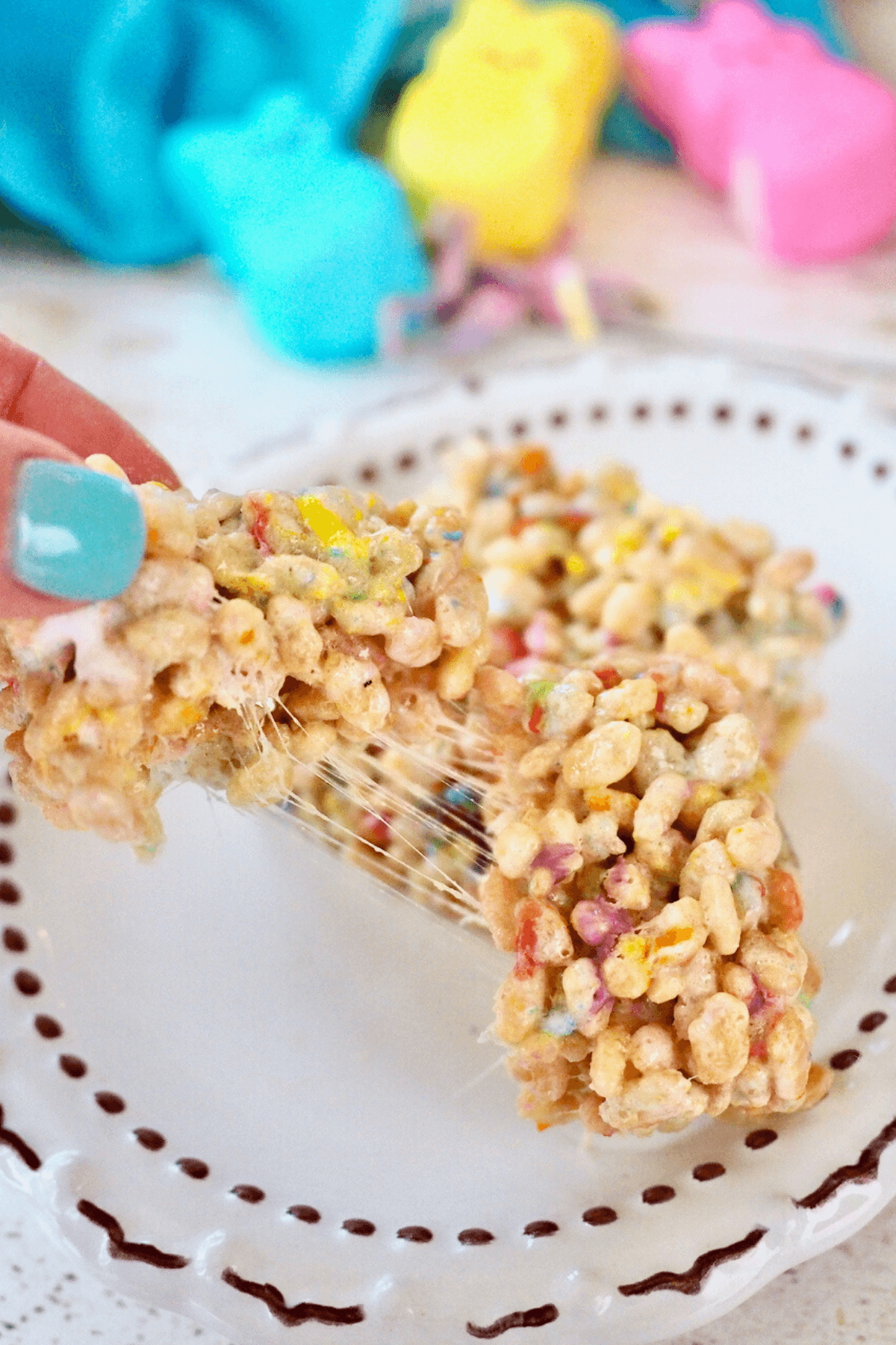 Hand pulling apart a gooey, warm Peeps Rice Krispie Treats on egg shaped plate.