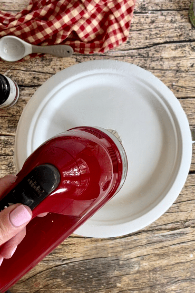 Paper plate splatter shield on top of bowl with hand mixer. 