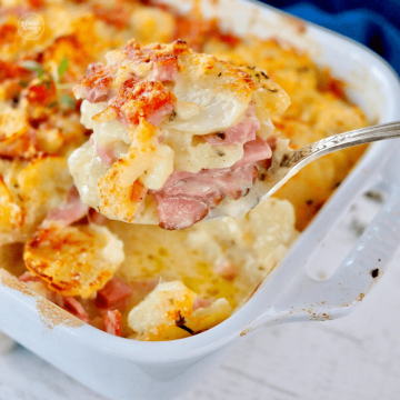 Instant Pot Scalloped Potatoes with Ham in baking dish, hand scooping out portion.