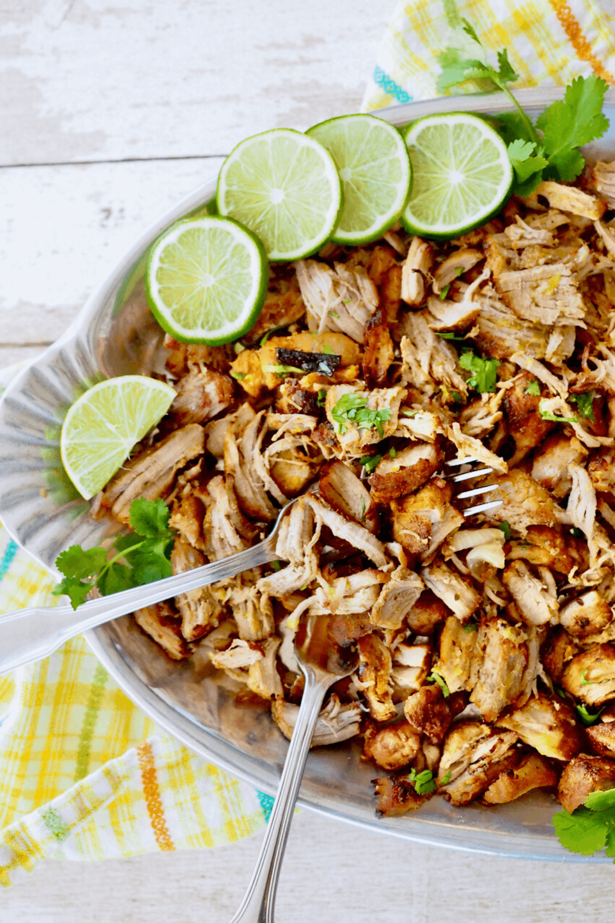 Instant Pot Carnitas shredded pork on platter with lime wedges and cilantro.
