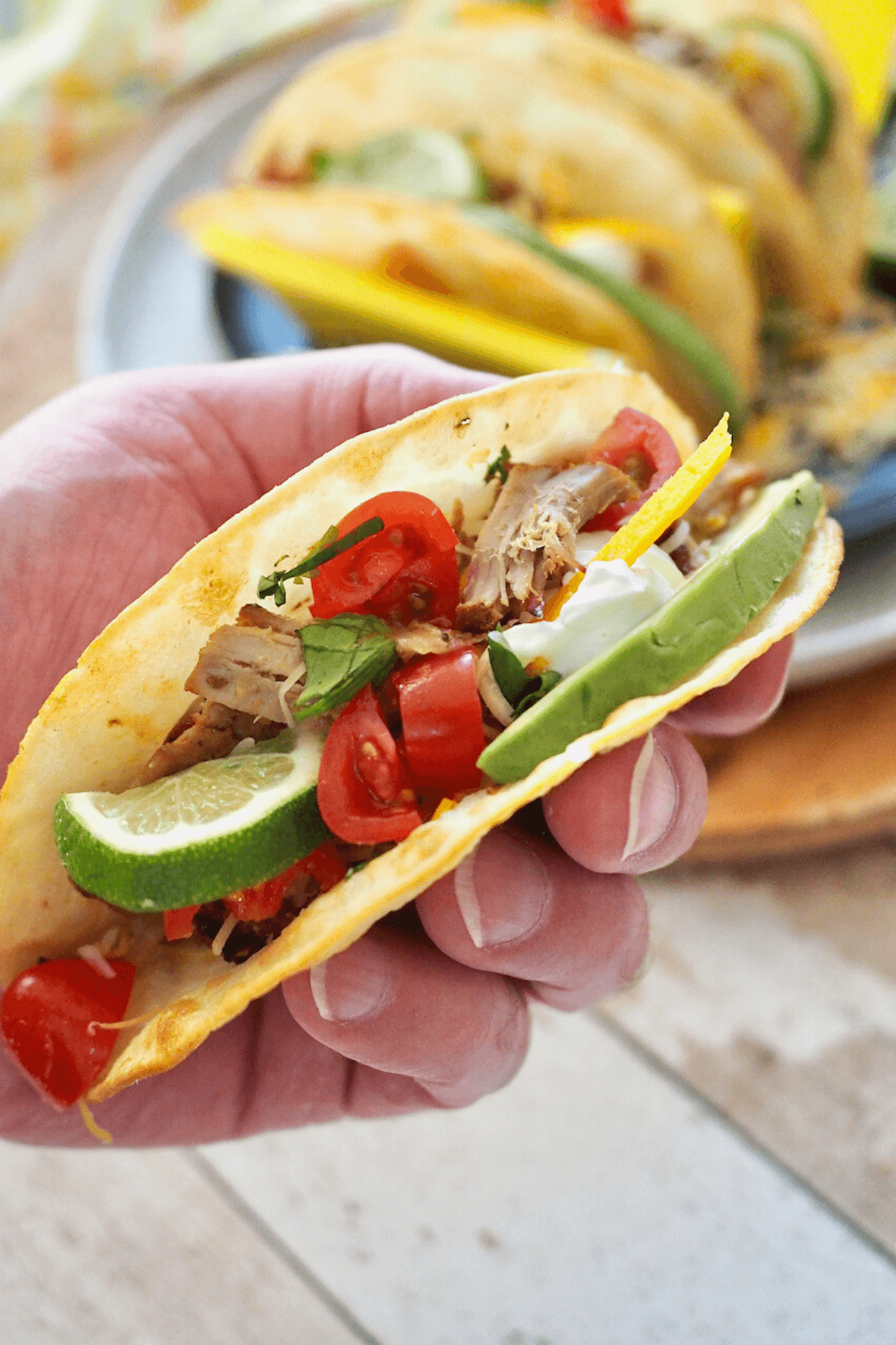 Mans hand holding soft taco filled with pork carnitas and more tacos in background.